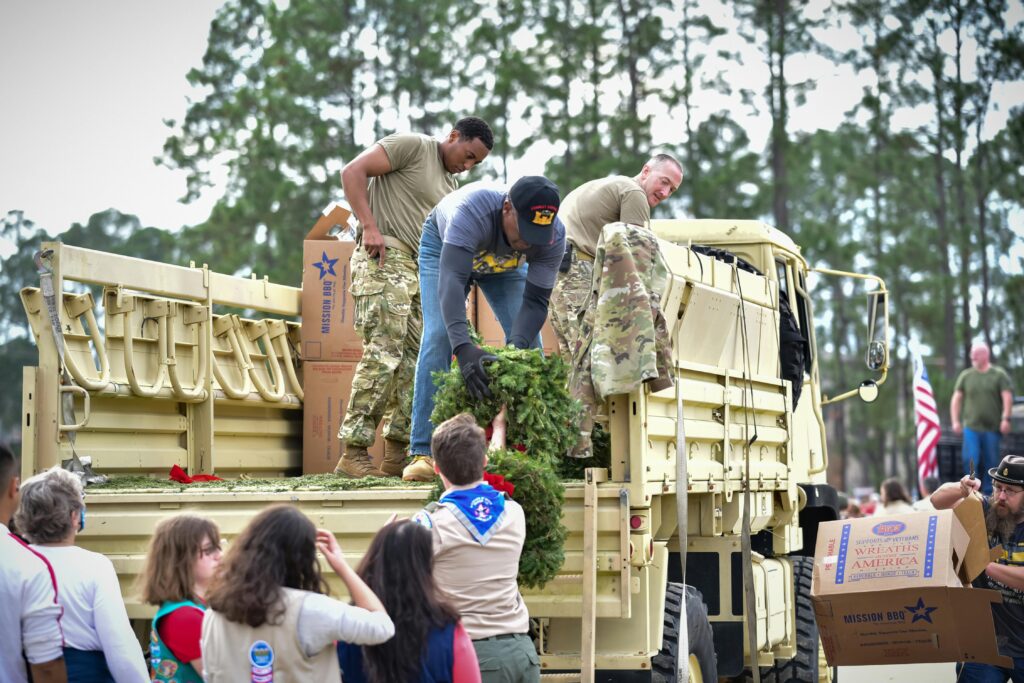 Volunteers of various ages load wreaths onto a military truck, promoting unity and teamwork.